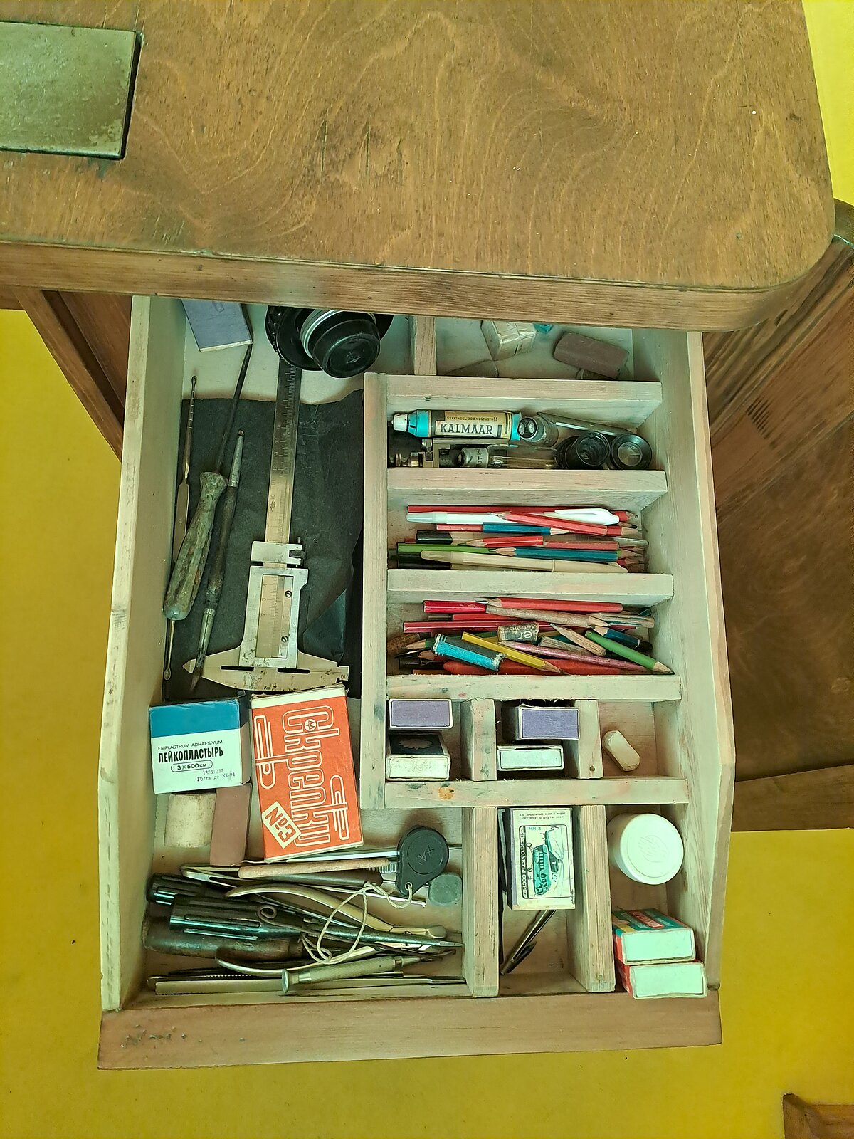 Augšējā atvilktne ar iedaļām. Redzami nelieli priekšmeti, tai skaitā rakstāmpiederumi, preparēšanas instrumenti, bīdmērs, mikroskopēšanas okulāri un spuldze, lupa, nelielas kārbiņas īpaši sīkiem priekšmetiem Augšējā atvilktne ar iedaļām. Redzami nelieli priekšmeti, tai skaitā rakstāmpiederumi, preparēšanas instrumenti, bīdmērs, mikroskopēšanas okulāri un spuldze, lupa, nelielas kārbiņas īpaši sīkiem priekšmetiem